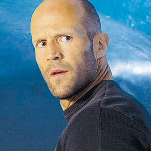 A bald man with stubble wearing a dark sweater looks over his shoulder with a surprised or concerned expression, set against a blue background.