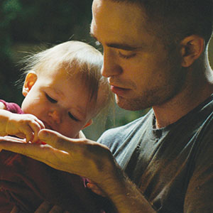 A man gently holds a baby who is focused on exploring his hand, creating a tender and intimate moment between them.