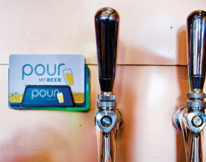 A glass is being filled with beer from a tap on a wall. There are two taps visible, and a sign in the background says pour my beer with an image of a beer glass.