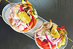 Two small dishes filled with ceviche, garnished with lime wedges, sliced red onions, red chili, and colorful vegetables, served on a metal tray atop a dark surface.