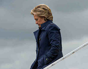 A person wearing a dark blue coat walks down airplane stairs against a cloudy gray sky, looking downward with a serious expression.
