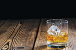 A glass of whiskey with ice sits on a rustic wooden surface against a dark background.