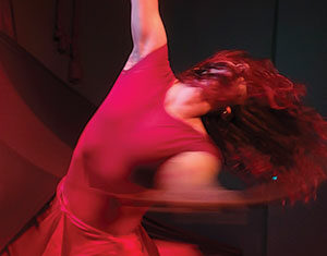 A person in a flowing red dress dances passionately, their hair and dress swirling with their movement, creating a dynamic and expressive scene.