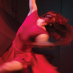 A person in a flowing red dress dances passionately, their hair and dress swirling with their movement, creating a dynamic and expressive scene.