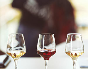 Three wine glasses filled with different types of wine—white, red, and rosé—are arranged in a row on a white surface with a blurred background.