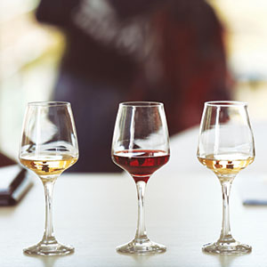 Three wine glasses filled with different types of wine—white, red, and rosé—are arranged in a row on a white surface with a blurred background.