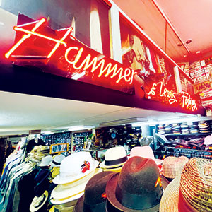 A brightly lit hat store displays various hats on racks, with a red neon sign reading Hats and shelves of hats along the wall in the background.