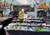 A person stands behind a table filled with colorful pop-up greeting cards under a white canopy at an outdoor market. A holidaypop banner hangs at the back and other vendors’ booths are visible nearby.