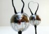 Two reflective, metallic oval sculptures with long, black, wire-like antennae, standing upright against a plain white background. The surfaces reflect the room and a person taking the photo.