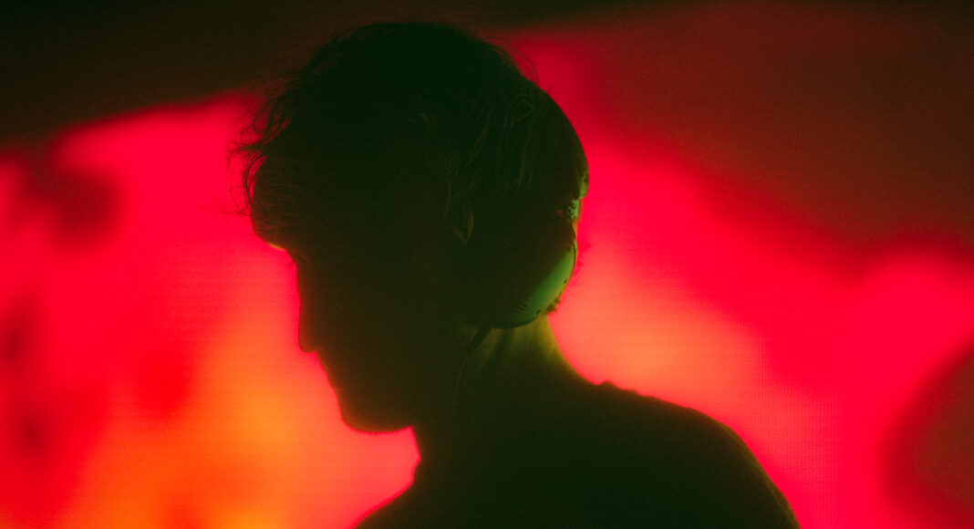 A person wearing headphones is shown in silhouette against a vibrant, abstract red and yellow background. The lighting creates a dramatic effect, highlighting the outline of their head and shoulders.