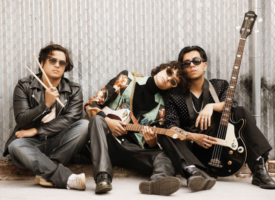 Three musicians lounging against a wall