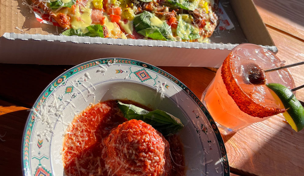 Closeup of a meatball, a drink, and the edge of a pizza