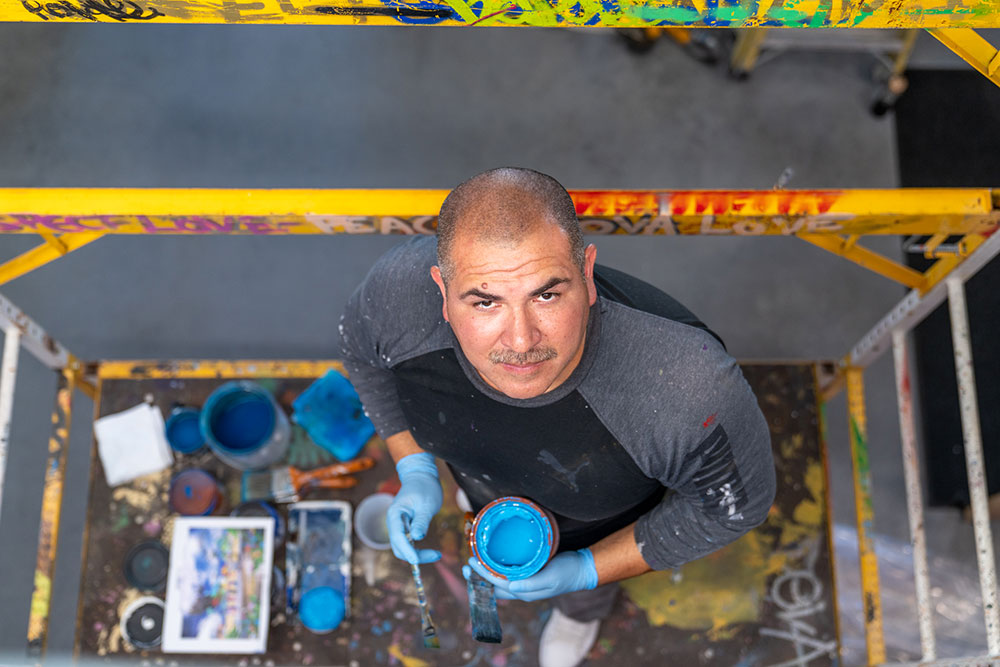 Man on a scaffold holding paint and a brush