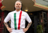 Restaurateur standing in front of one of his restaurants wearing an apron with the colors of the Italian flag