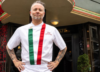 Restaurateur standing in front of one of his restaurants wearing an apron with the colors of the Italian flag