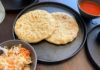 Two pupusas on a plate with bowls of cabbage and red salsa on the side