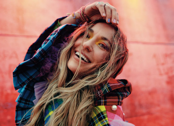 Woman with brightly colored hair posing in front of a painted brick wall