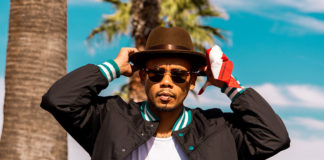 Man in sunglasses, his hands touching his hat, standing by palm trees