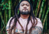 Photo of man with his arms folded, with tattooed arms and dreadlocks