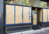Storefront with windows taped up and a plaque on the side