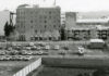 Black and white photo of parking lot in front of an old hotel