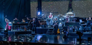 Large ensemble of musicians playing on a stage with holiday lights
