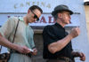 Two men walking down a street with signs on the buildings in Spanish