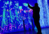Man in silhouette looking at neon-bright images of flowers projected on the wall