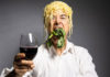 Man with a pile of noodles on his head toasting the camera with a glass of wine
