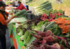 People at a farmers market with tables filled with produce