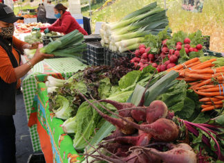 People at a farmers market with tables filled with produce