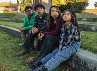 Four people sitting on a curb in front of a school