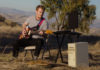 Guitar player outdoors on a hillside with instruments and other equipment