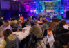People sitting at long tables in a room with colorful lighting