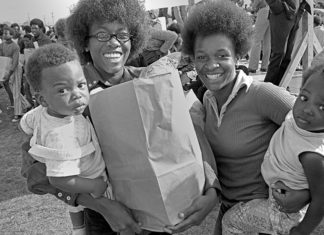 Black and white archival photo of African American families holding bags of food