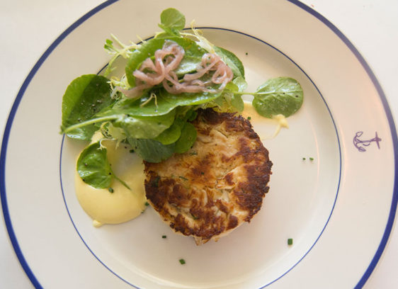 Overhead view of crab cake and salad on a white plate decorated with a small blue anchor