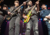 Four men standing close together and playing guitars onstage