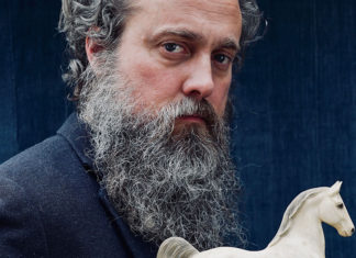 Bearded man against a dark background holding onto a toy horse
