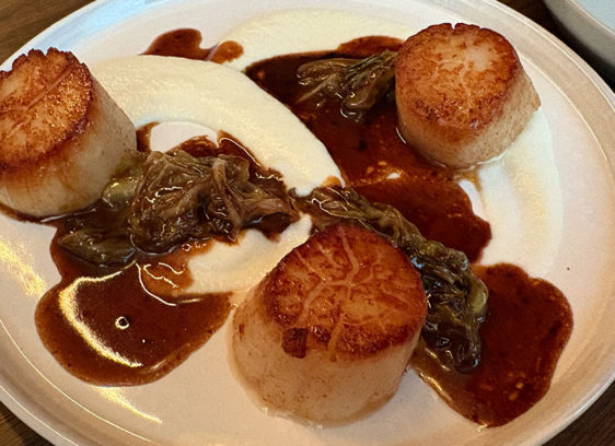 Plate of food on a table with three scallops