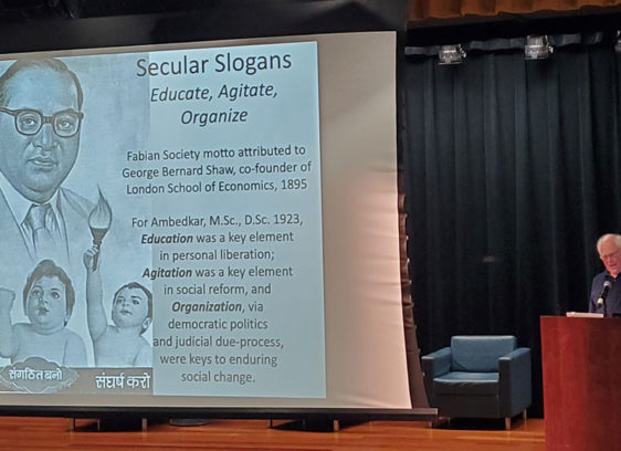 man at podium next to a large slide projection
