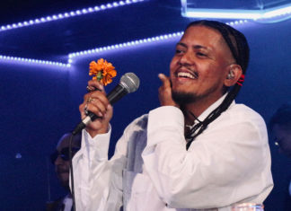Man singing into a microphone and holding a marigold