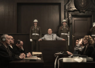 Man taking the stand, military police on either side of him, with other court personnel also in the courtroom