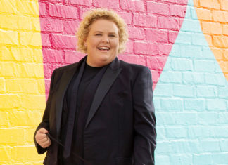 Woman wearing a black suit standing in front of multicolored brick wall