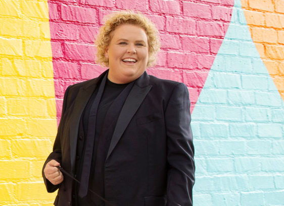 Woman wearing a black suit standing in front of multicolored brick wall