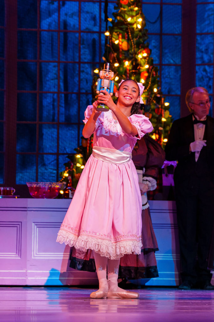 Girl wearing an old-fashioned dress and ballet shoes, holding a carved nutcracker toy
