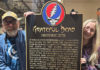Two people on either side of a plaque, holding it upright. Plaque has the Grateful Dead’s logo on it