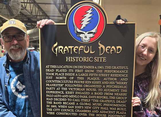 Two people on either side of a plaque, holding it upright. Plaque has the Grateful Dead’s logo on it