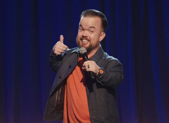 Man talking into a microphone and performing on a stage