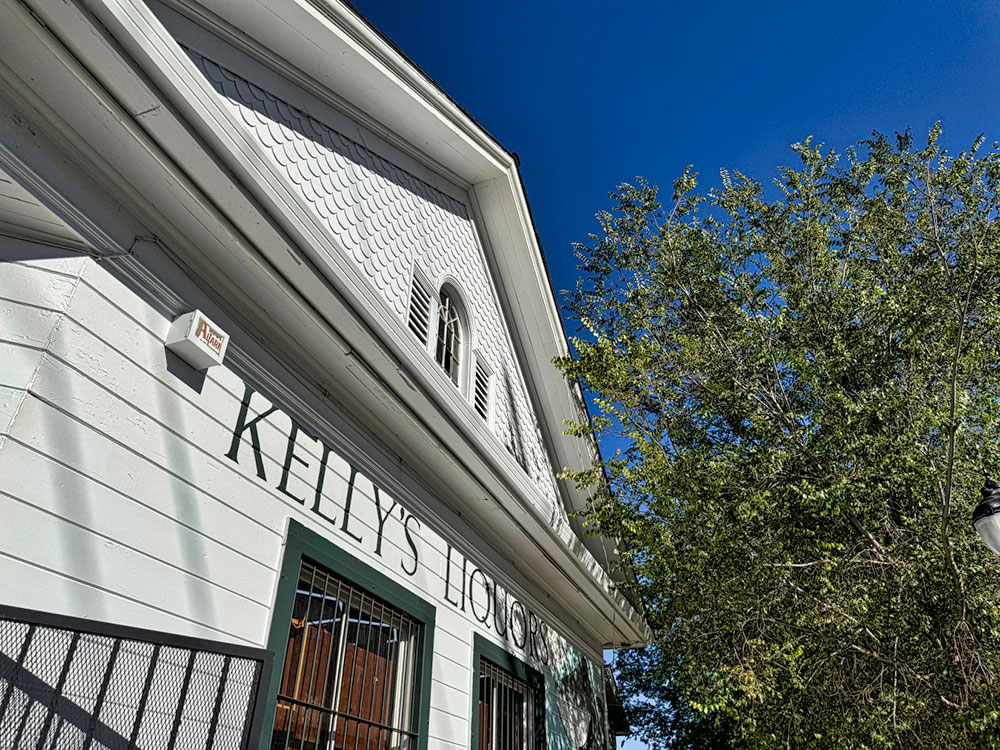 Front of a historic wooden building with Kelly's Liquors painted in black on white background