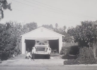 Archival black-and-white photo of an open garage with a car being worked on